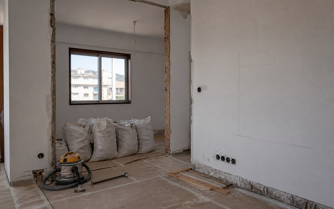 Divisória parcialmente removida com pavimento protegido e resíduos organizados em sacos de obra